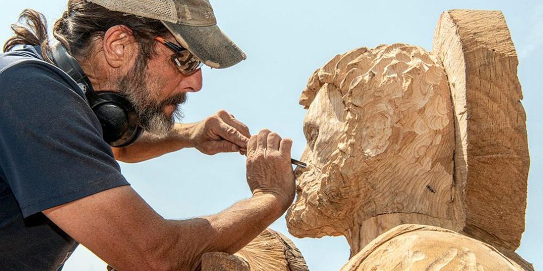 A man standing next to a large wood sculpture